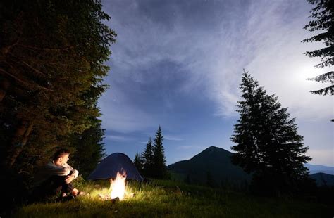 O cara está sentado perto do fogo no fundo da tenda e da floresta de