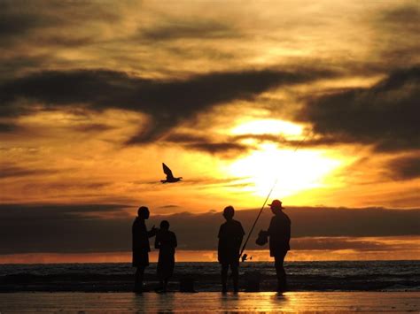 Silhueta de pessoas pescando na praia contra o céu nublado durante o