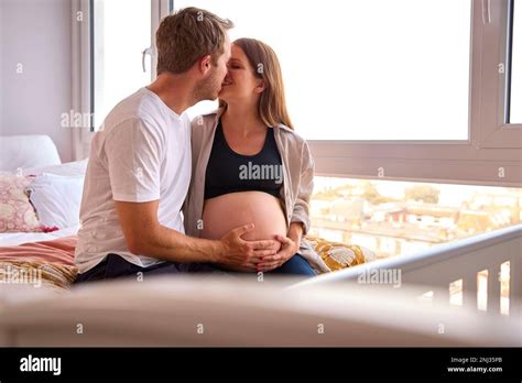 Loving Couple At Home Sitting On Bed With Man Touching Pregnant Woman S