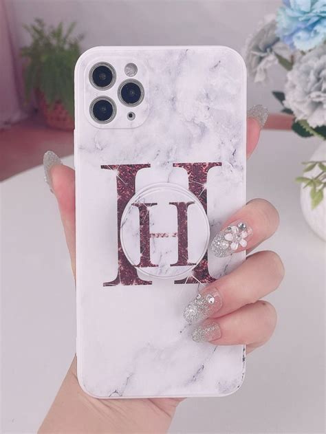 A Woman Holding Up Her Phone Case With The Letter D On It And Diamond Studs