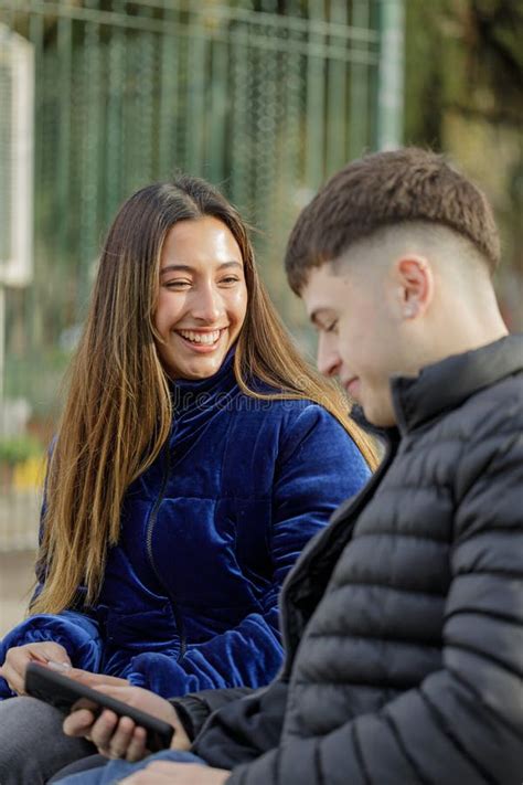 Chica Latina Sonriendo Sentada En Un Banco De Plaza Con Su Novio Foto De Archivo Imagen De