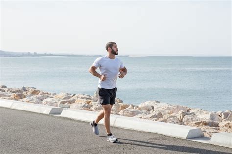 Serious muscular man running on seaside road Photo | Free Download