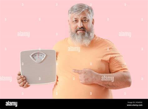 Overweight Happy Mature Man Pointing At Scales On Pink Background