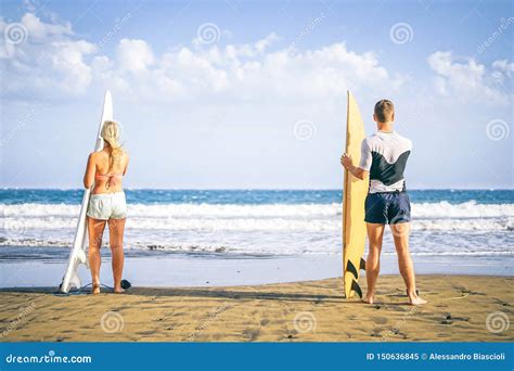 Young Couple Of Surfers Standing On The Beach With Surfboards Preparing