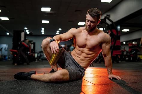 Premium Photo Very Muscular Sporty Guy Drinking Protein In Dark Red Background With Naked