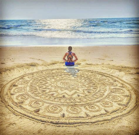 A Woman Sitting On The Beach Looking At An Intricate Design In The Sand