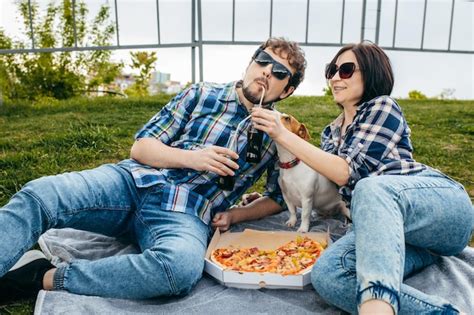 Familia joven con su perro sentado en el césped y comiendo pizza al