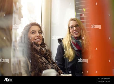 Blond And Brunette Female Friends Wearing Coats Talk In Public Space