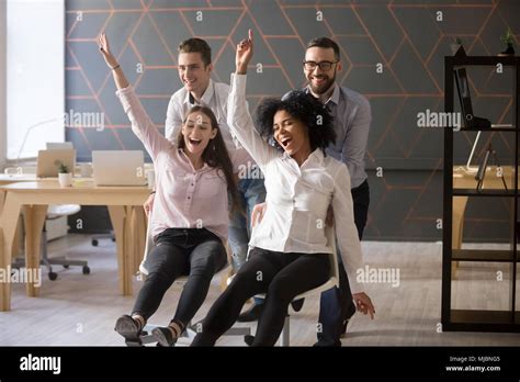 Excited Diverse Colleagues Having Fun Riding Oh Chairs In Office Stock