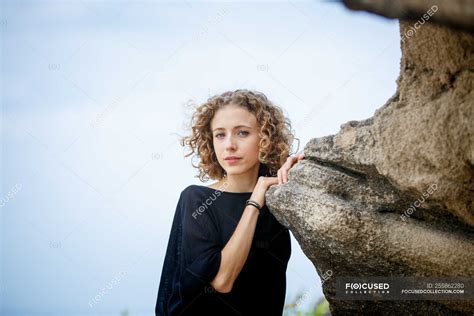 Young Serious Woman Leaning On Rock In Nature And Looking At Camera