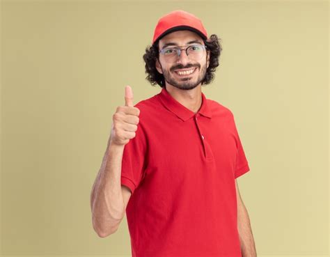 Sonriente joven caucásico repartidor en uniforme rojo y gorra con gafas