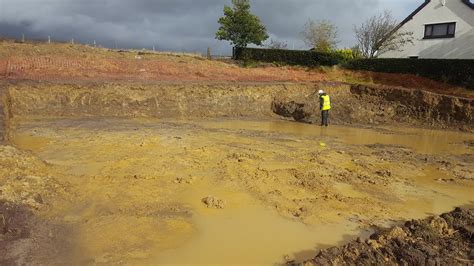 A Man Standing On Top Of A Muddy Field Next To A House And Dirt Hill