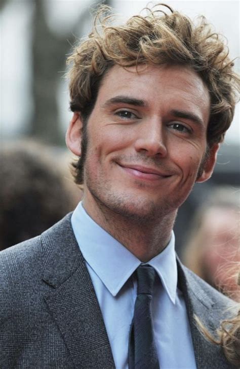 A Man With Curly Hair Wearing A Suit And Tie Smiling At The Camera