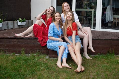 Group Of Young Smiling Gorgeous Barefoot Women Sitting On Wooden Veranda Near Green Grass