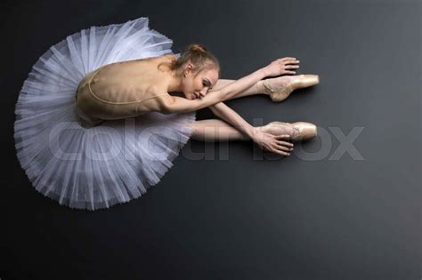 Young Graceful Ballerina Sitting On The Floor On A Black Background In