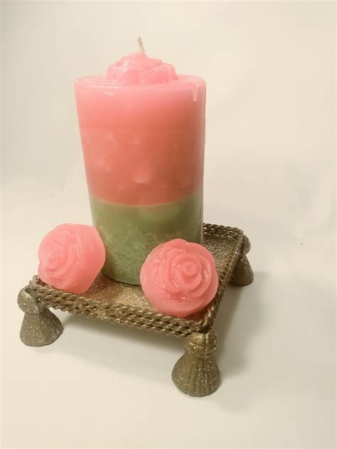 A Pink And Green Candle Sitting On Top Of A Metal Tray With Two Small Roses