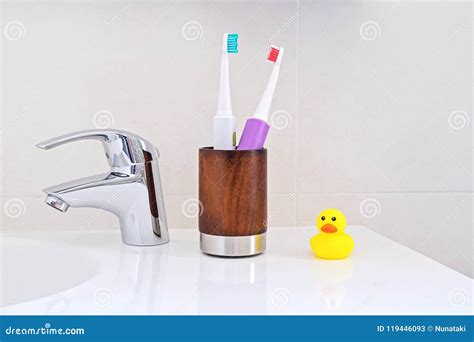 Two Electric Toothbrushes In Wooden Glass On Sink In The Bathroom Stock