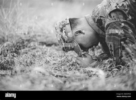 Grayscale Shot Of An American Soldier Kneeling And Praying On A Dry