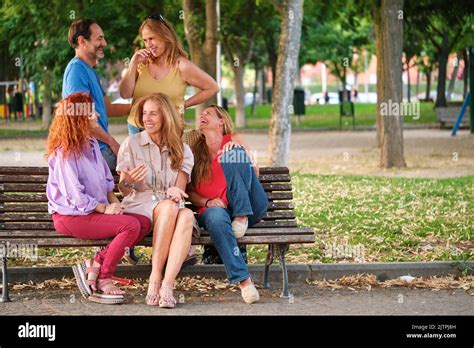 Five Mature Adults Talking And Laughing Sitting On A Bench In A Park