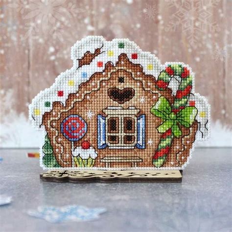 A Cross Stitch Gingerbread House Ornament On A Wooden Stand With