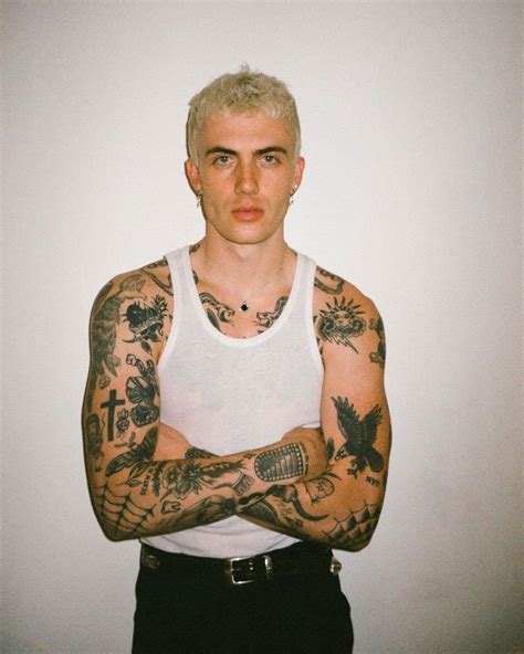 A Man With Tattoos On His Arms And Chest Standing In Front Of A White Wall