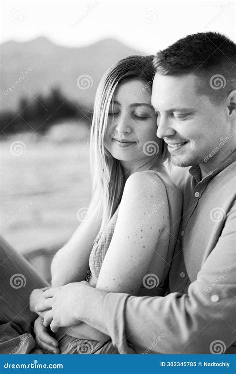 Man Hugs Woman From Behind While Sitting With Her On The Seashore