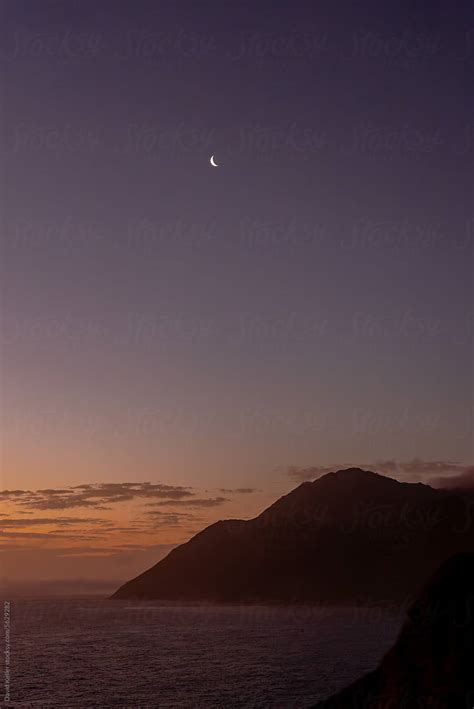 A Sliver Of The Moon Radiates Above A Cloudy Sunset On The Coast