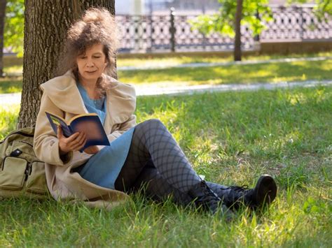 Premium Photo Middleaged Woman Sitting On The Grass And Reading Book