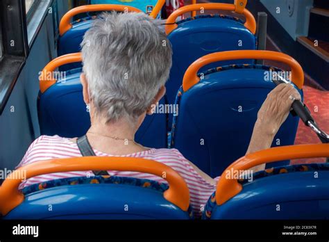 Senior Citizen Lady Wearing A Face Mask Sitting On A Bus Journey Sitting Apart During Social