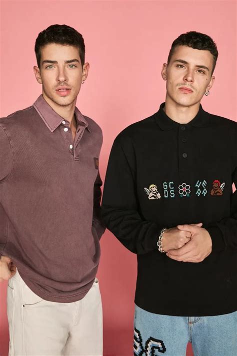 Two Young Men Standing Next To Each Other In Front Of A Pink Wall Wearing Sweaters