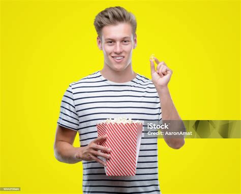 Young Handsome Blond Man Eating Popcorn With A Happy Face Standing And