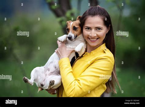 Young Woman In Yellow Jacket Holding Her Jack Russell Terrier Dog On