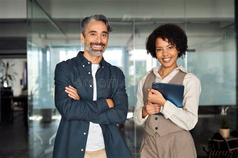 Two Diverse Business Partners Standing In Office Looking At Camera