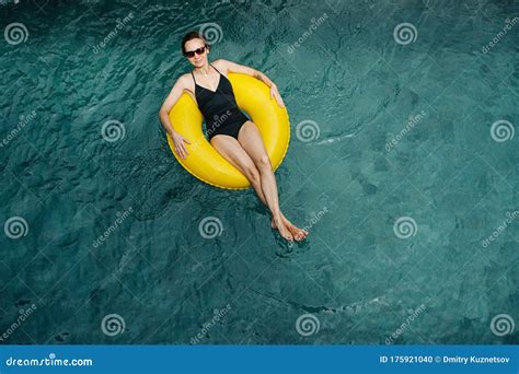 Girl In A Black Swimsuit Lying On A Rubber Yellow Circle In The Pool