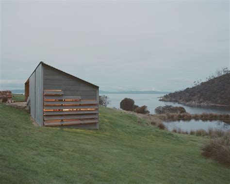 A Building Sitting On Top Of A Lush Green Hillside Next To A Body Of Water