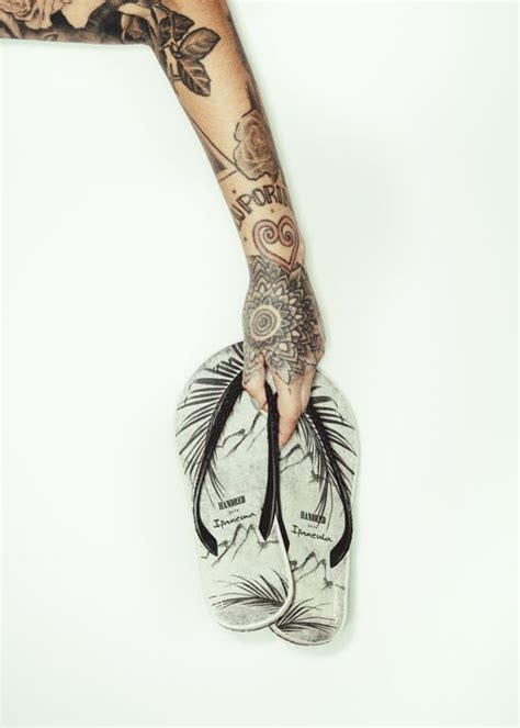 A Person With Tattoos On Their Arm Holding Onto A Pair Of Flip Flops