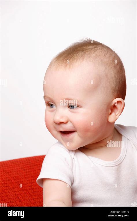 Happy Six Month Old Baby Boy Sitting On A Red Sofa Making Facial