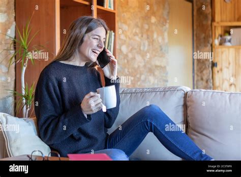 Happy Young Brunette Woman Talking On The Mobile Sitting On The Sofa At