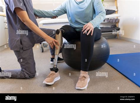 Physical Therapist Adjusting Prosthetic Leg For Patient Sitting On Exercise Ball