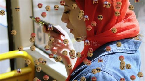 Animation Of Falling Emojis Over Woman In Hijab Using Smartphone Stock