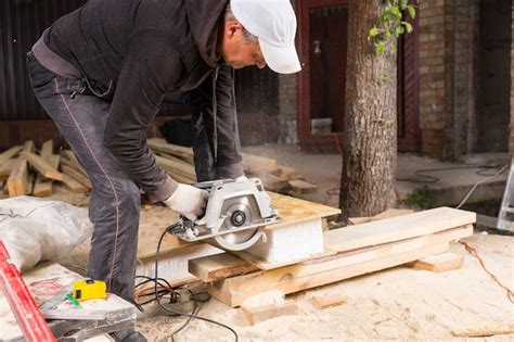 Premium Photo Man Using Hand Held Power Saw To Cut Planks Of Wood For