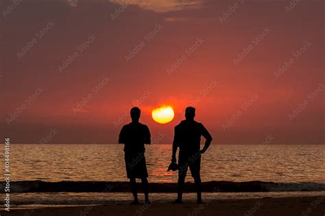 Silueta De Dos Hombres Contemplando El Atardecer En La Playa De Los