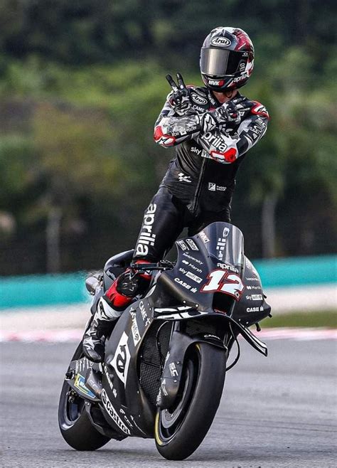 A Man Riding On The Back Of A Motorcycle Down A Race Track With Trees