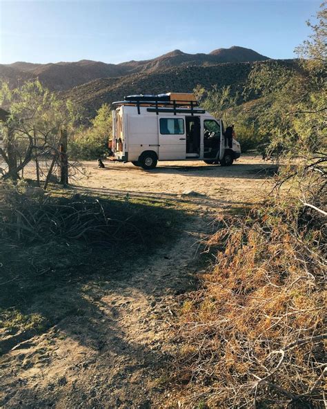 A Camper Van Parked In The Middle Of A Dirt Road With Mountains In The