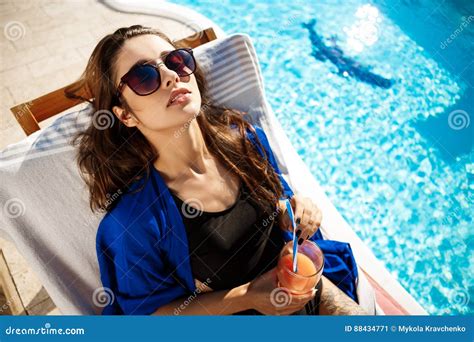 Beautiful Girl Drinking Cocktail Lying On Chaise Near Swimming Pool