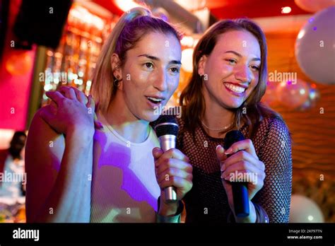 Two Happy Caucasian Female Friends Singing Karaoke At A Nightclub Bar