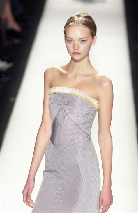 A Woman Walking Down A Runway In A Gray Dress