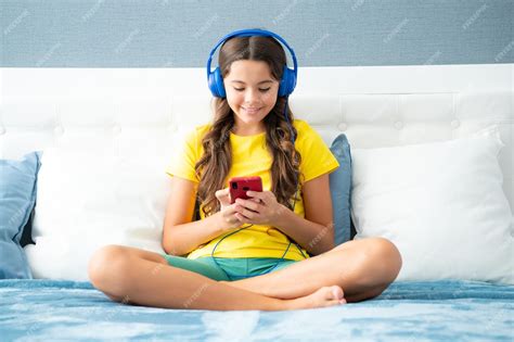 Menina Adolescente Feliz Usando Fones De Ouvido Assistindo Vídeos No Smartphone Sentado Na Cama