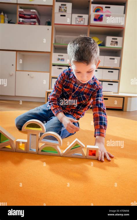 Boy Lining Up Wooden Toy Shapes On Carpet In Kindergarten Stock Photo