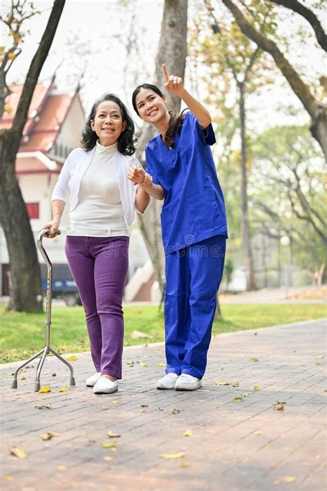 Caring Asian Female Caregiver Enjoys Talking And Walking In The Park